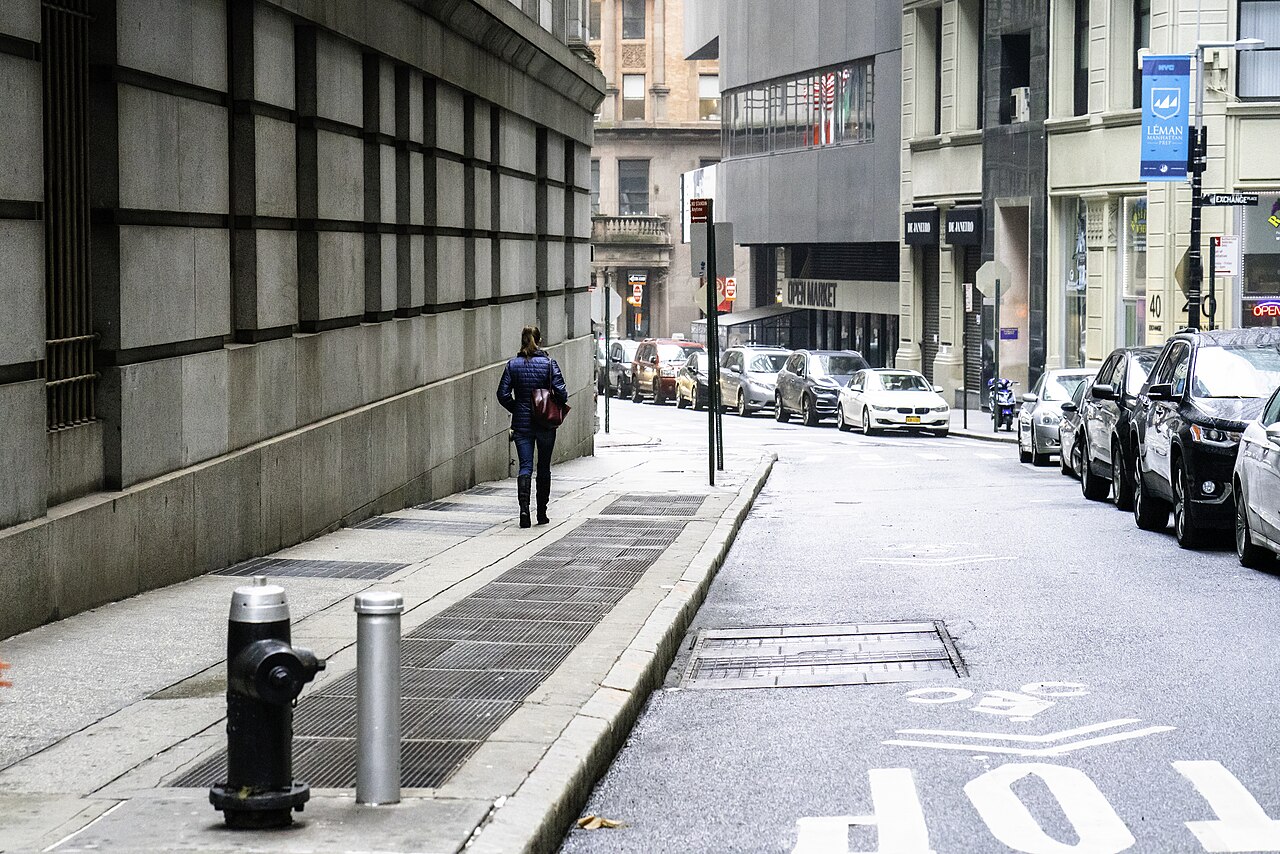 Une rue étroite bordée de gratte-ciel, vide de circulation et de piétons, sous un ciel dégagé.